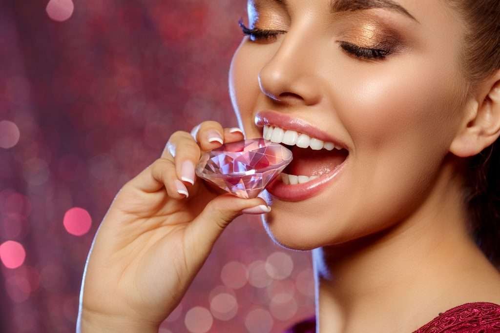 female model smiling and biting down on a large pink diamond