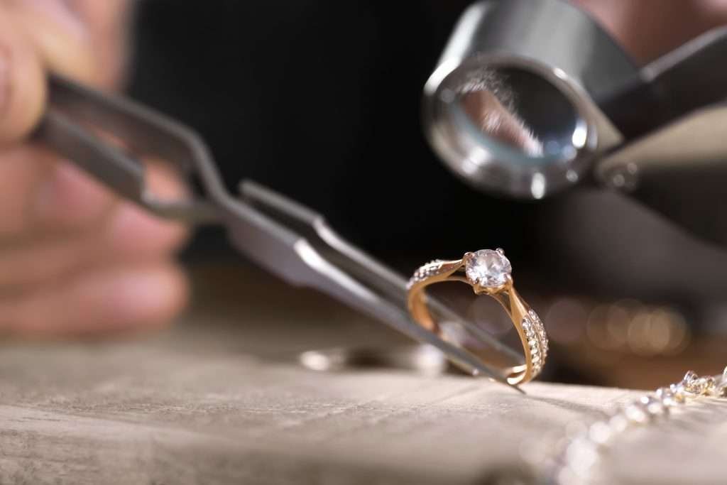 diamond ring being examined with tweezers and a jeweler loupe