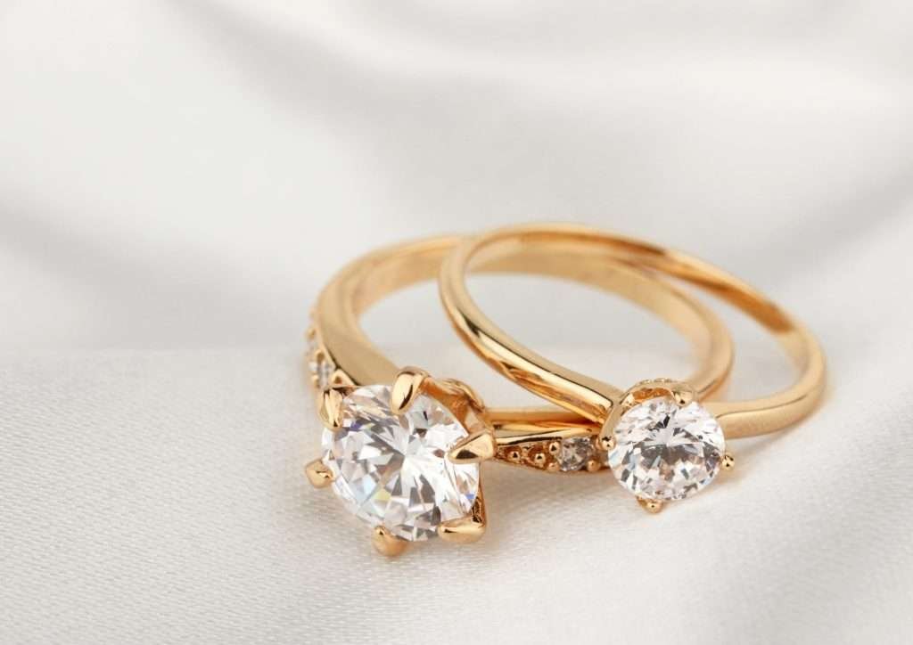 two gold round diamond engagement rings on white cloth
