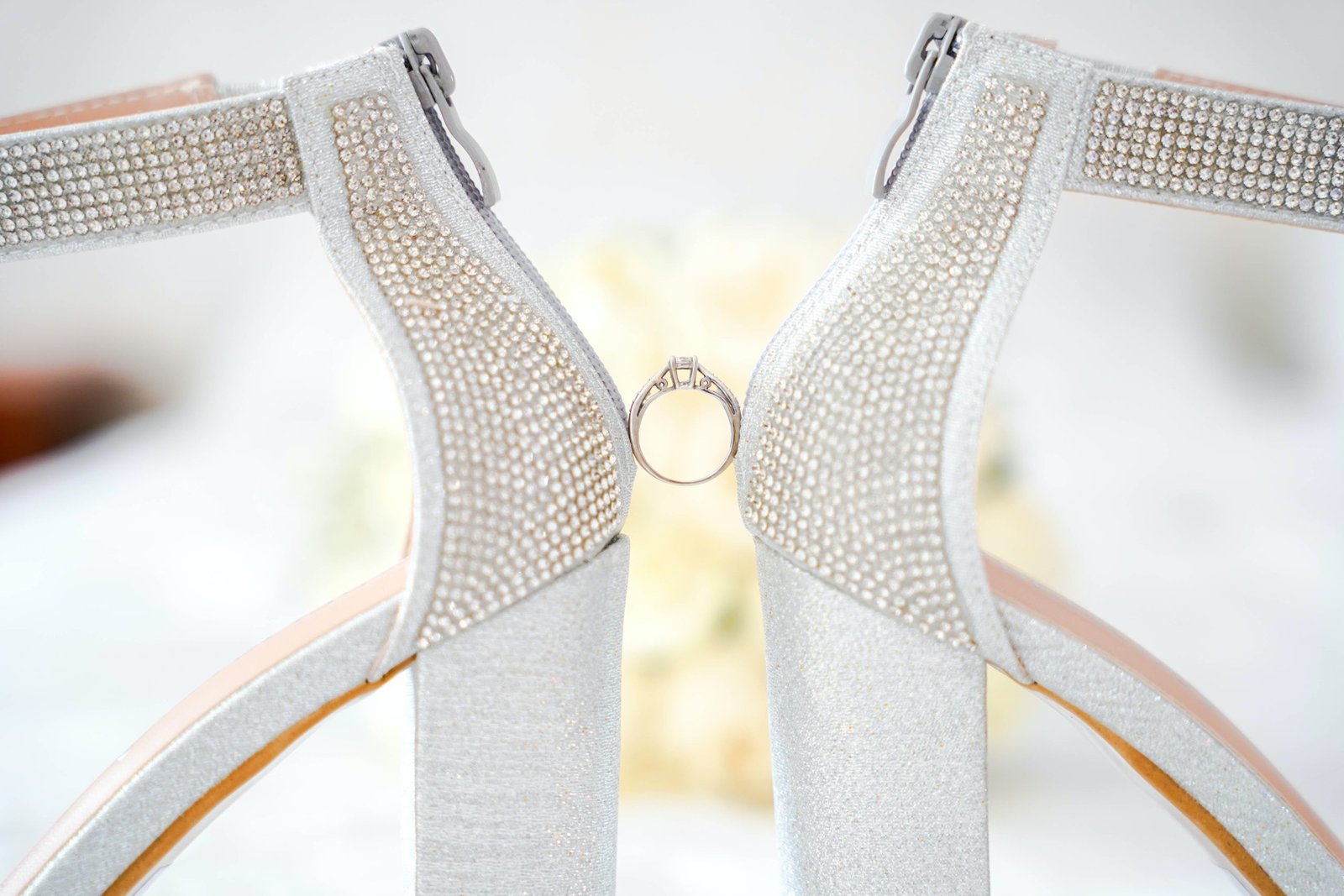 white wedding shoes holding diamond engagement ring